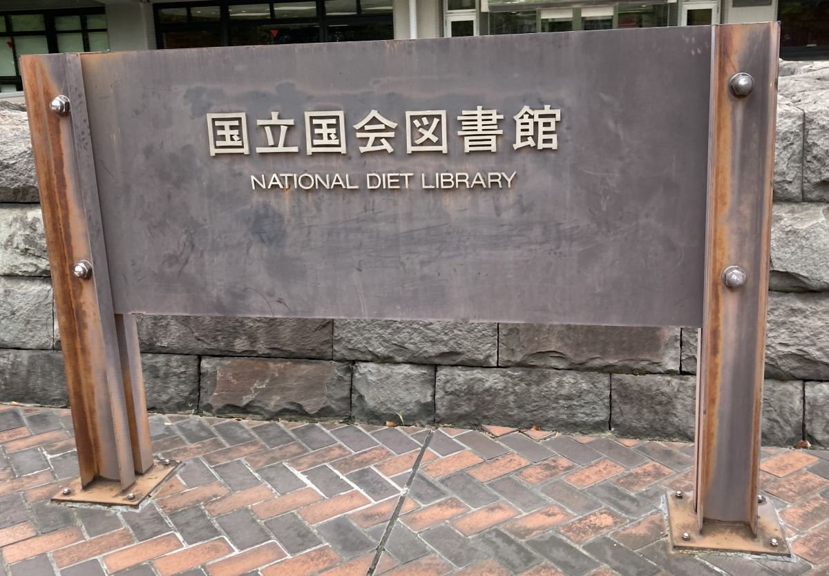 国立国会図書館の看板です。黒ずんだ銅の看板には、国立国会図書館と上部に書かれていて、下部にはNational Diet Libraryと英語の大文字で書かれています。